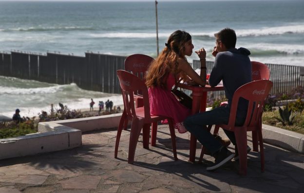 Pareja en Tijuana, en el punto más occidental de la frontera entre México y Estados Unidos, con el muro que divide ambos países detrás.