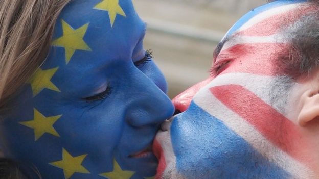 Una mujer con el rostro pintado con la bandera de la UE y un hombre con el suyo con la bandera de Reino Unido se besan