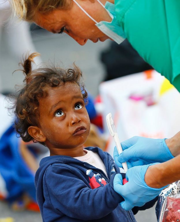 A young migrant girl from Iraq watches a Red Cross nurse during the registration outside the main station in Munich, Germany, Tuesday, Sept. 1, 2015