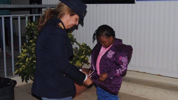 ஔமோக்கை கவனித்துக் கொள்ளும் காவல்துறை கண்காணிப்பாளர் மரியா வால்பே, (சிறுமியின் முகம் மறைக்கப்பட்டுள்ளது)