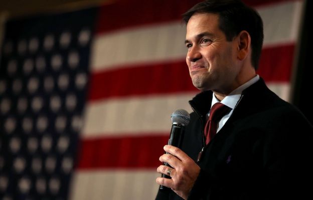 Marco Rubio standing in front of an American flag