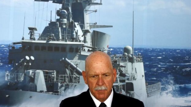 Commander of the US Pacific Fleet Admiral Scott Swift sits in front of a large poster of an Australian Navy frigate in Sydney (15 December 2015)