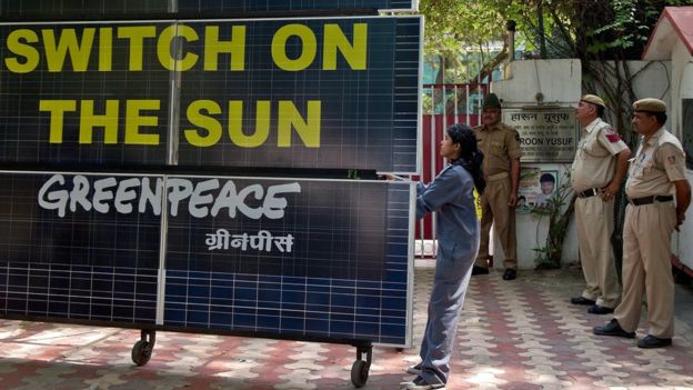 Indian policemen look on as a Greenpeace activist blocks the entry to the residence of Delhi's Power Minister Haroon Yusuf with a bank of solar panels in New Delhi