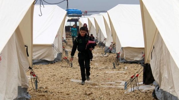 Displaced Syrians fleeing areas in the northern embattled province of Aleppo, walk past tents at the Bab al-Salama camp, set up outside the Syrian city of Azaz on Syria's northern border with Turkey (12 February 2016)