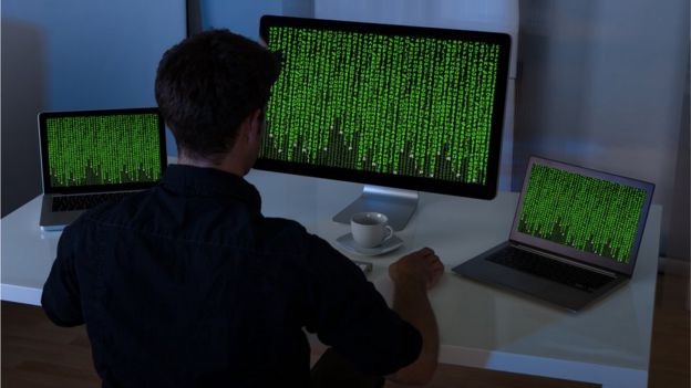 hacker dándole la espalda a la cámara frente a una computadora llena de cifras.