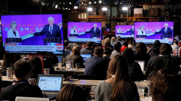 Journalists watch Democratic US presidential candidates Hillary Clinton (L) and Senator Bernie Sanders debate on video screens