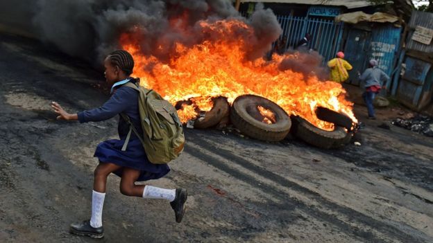A schoolgirl runs past a burning barricade in Kibera slum, Nairobi, Kenya - Monday 23 May 2016