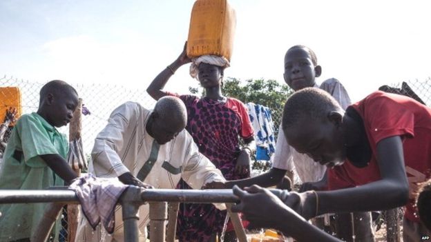 A woman carrying a bucket of water on her head looks on as refugees gather water at the Tomping Internally Displaced Persons (IDP) camp in Juba on July 2, 2014.