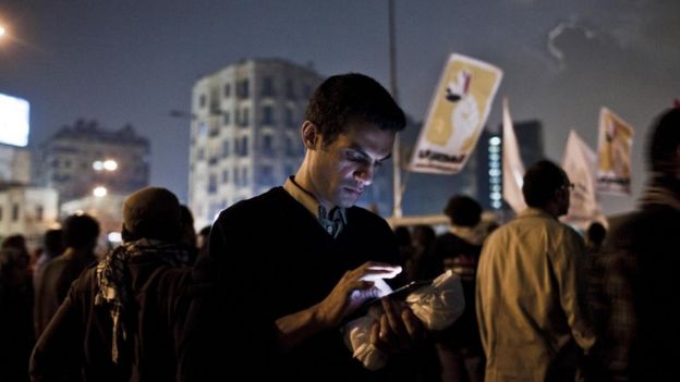 Un joven mira su teléfono inteligente durante unas protestas de la Primavera Árabe