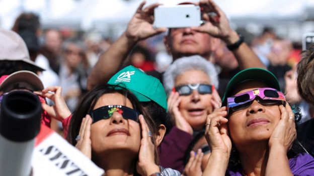 People look through eclipse viewing glasses, telescopes or photo cameras on the Indian Ocean island of La Reunion.