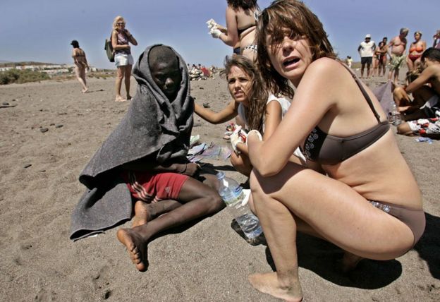 Tourists help a migrant boy on La Tejita beach, Tenerife