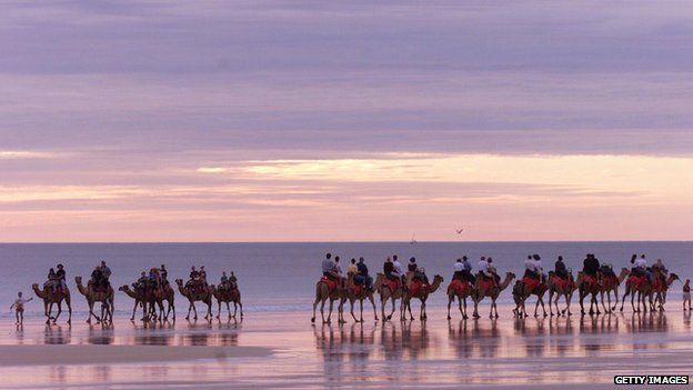 Tourists ride camels along Broome's Cable Beach, Western Australia