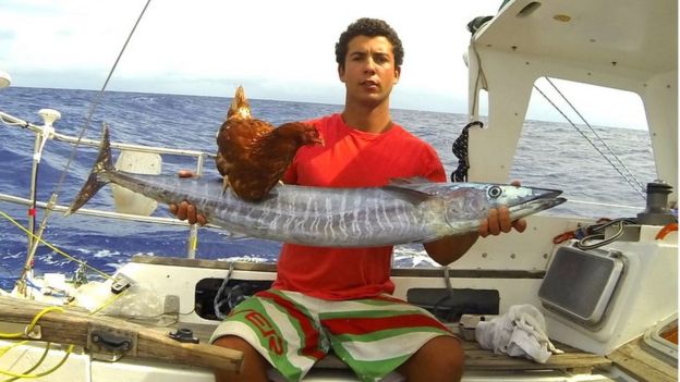 Sailor Guirec Soudee with a fish he caught, and Monique the hen standing on top of it