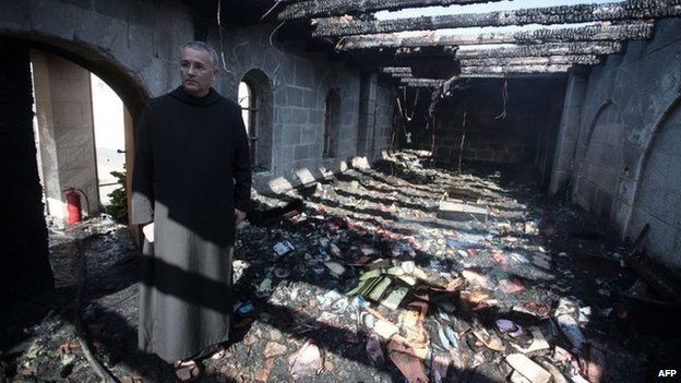 A priest inspects damage caused to the Church of the Multiplication of the Loaves and Fishes in Galilee, Israel, by an arson attack (18 June 2015)