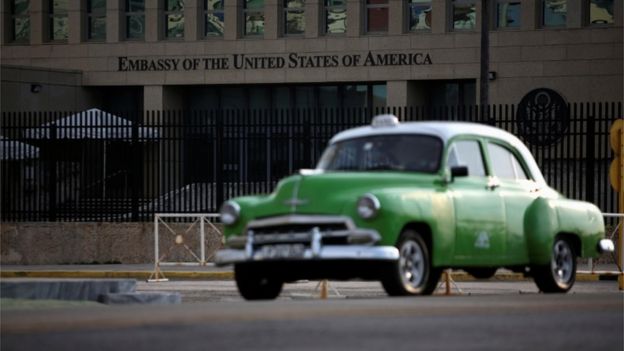 A green car driving past the US embassy in Havana