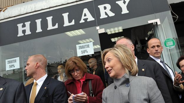 Then Secretary of State Hillary Clinton (C) smiles as she walks out of a store named in her honour in Pristina on 13 October 2010