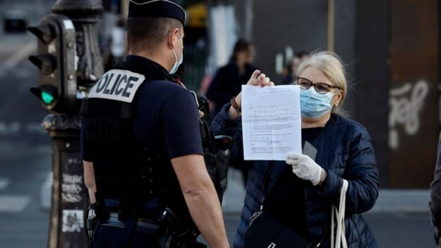 A police officer checks a woman"s self-certified note for being out before a two minute commemoration near the Notre-Dame Cathedral in Paris at 8 o"clock, on April 15, 2020