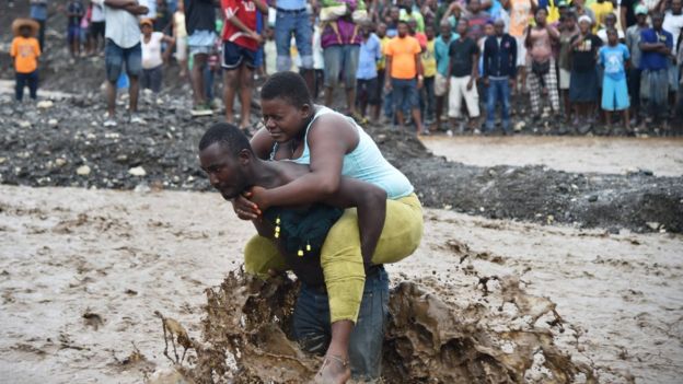 A man carries a woman across a river at Petit Goave where a bridge collapsed during the rains of Hurricane Matthew, south-west of Port-au-Prince, 5 October
