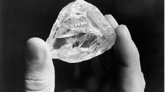 Diamante en bruto sostenido por dos dedos.