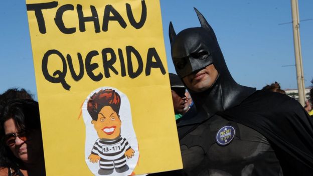 A man dressed as Batman holds up a sign reading 