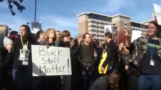 Protestors gather and hold signs, including one that reads "black staff matter"