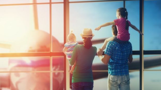 Una familia mirando un avión a través de la ventana del terminal aéreo