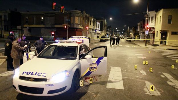 Police officers inspect a cruiser in which they allege an officer was ambushed