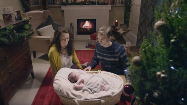 couple looking fondly at baby in Moses basket