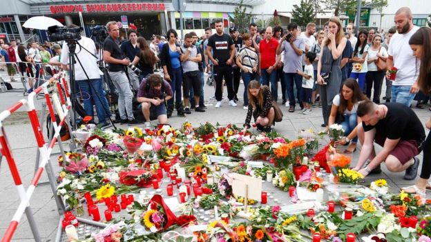 People look at the growing collection of flowers and candles for victims of the Munich shooting (23/07/2016)