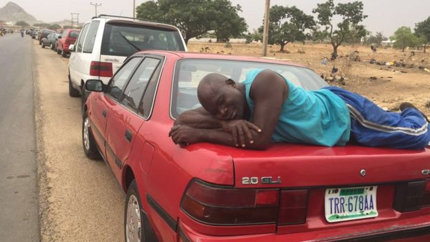 A man sleeping on the boot of his car in a fuel queue in Nigeria