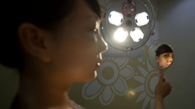 Girl holds mirror up to examine her face post-operation