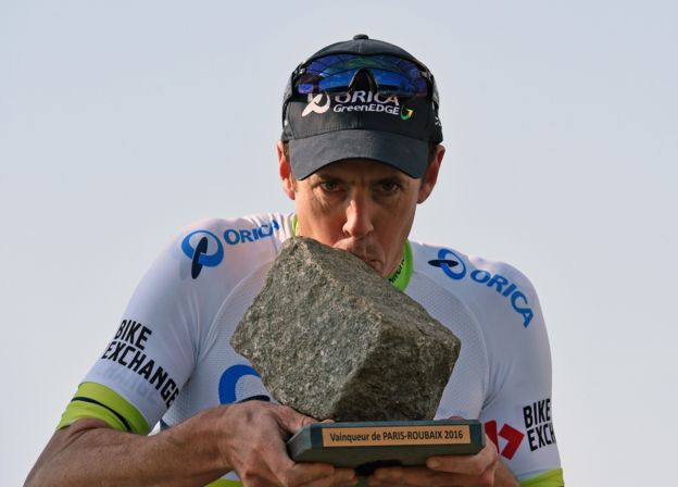 Ciclista besa un trofeo con forma de piedra.