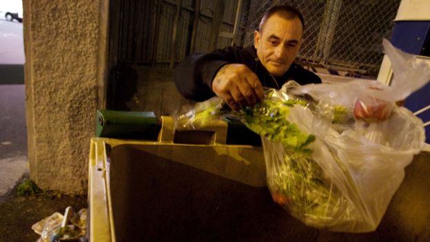 Un hombre rebusca comida en un cubo de basura