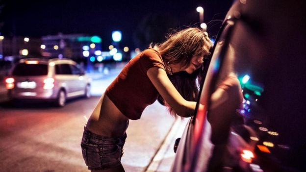 Una joven vendiendo sus servicios sexuales en la calle, habla con alguien en la ventanilla de un auto