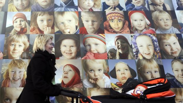 Mulher passa na frente de cartazes com fotos de crianças na Islândia