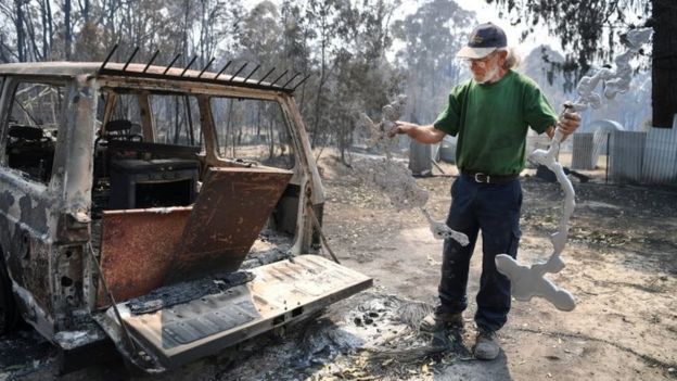 A man holding parts of melted metals surveys the destruction on his property in Torrington, NSW