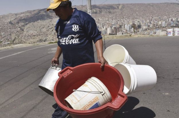 Hombre cargando muchos recipientes para recibir agua.