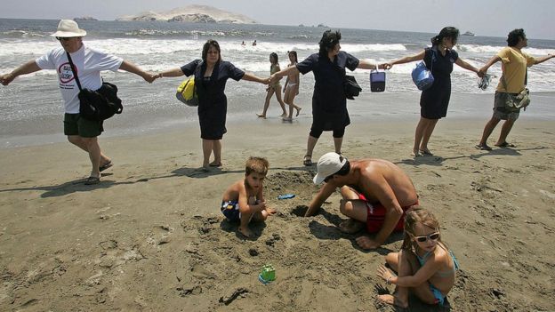 Mujeres vestidas como empleadas domésticas se toman de las manos en una playa de Perú