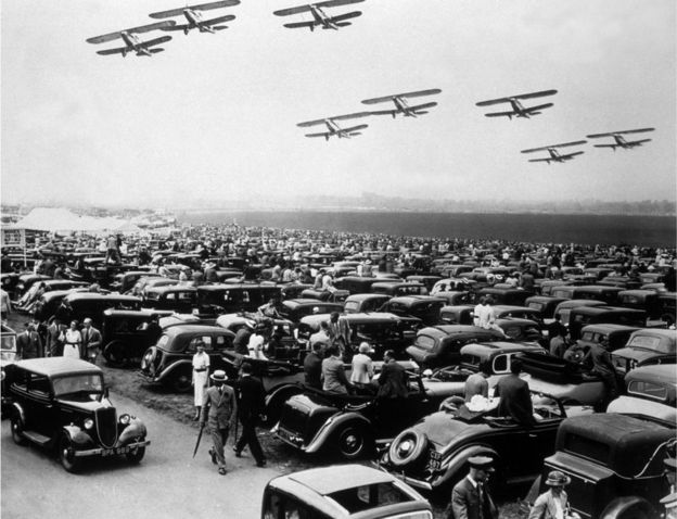 RAF aircraft flying over the packed car park, during the air display at Hendon, June 1936