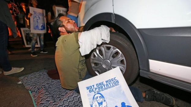 A protester locked himself to the van carrying Guadalupe Garcia de Rayos that is stopped by protesters outside the Immigration and Customs Enforcement facility, on 8 February in Phoenix
