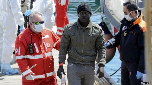 A migrant is helped as he disembarks from a Coast Guard boat in the Sicilian harbour of Palermo on 15 April 2015