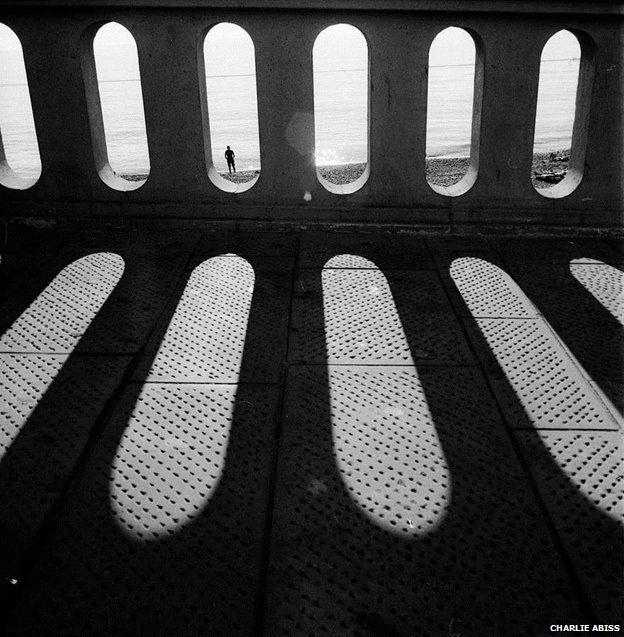 Black and white picture of man on beach framed through railings