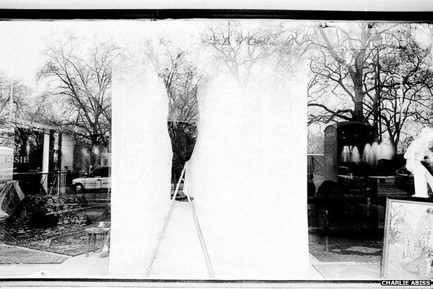 Window dresser through glass window (reflecting trees behind the camera)