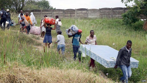 Foreign nationals carry their belongings before boarding a bus back to Zimbabwe from a temporary refugee camp in Chatsworth, south of Durban on April 19, 2015.