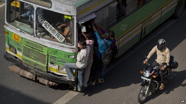 Commuters hang on the door of a crowded bus in New Delhi, India, Friday, April 10, 2015.