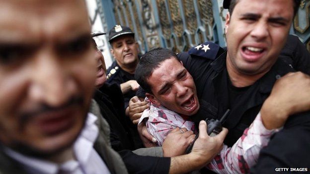 Egyptian policemen protect an opposition supporter during clashes with Muslim Brotherhood supporters outside the Ittihadiya presidential palace in Cairo (5 December 2012)