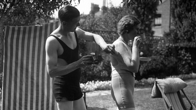 Man rubs suntan lotion on his wife's back, circa 1935