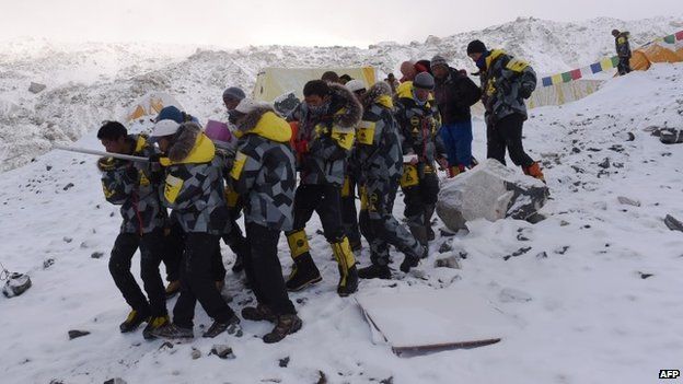 An injured person is carried by rescue members to be airlifted by rescue helicopter at Everest Base Camp (26 April 2015)