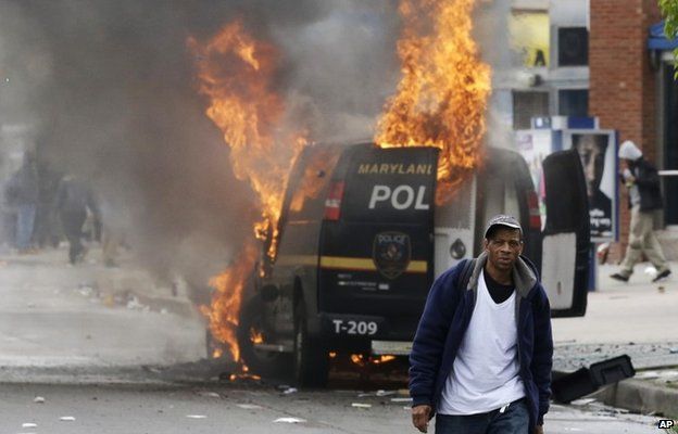 A man walks past a burning police vehicle