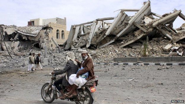 People ride on a motorcycle as they pass by a police headquarters destroyed by a Saudi-led air strike in Yemen"s northwestern city of Saada 7 May 2015